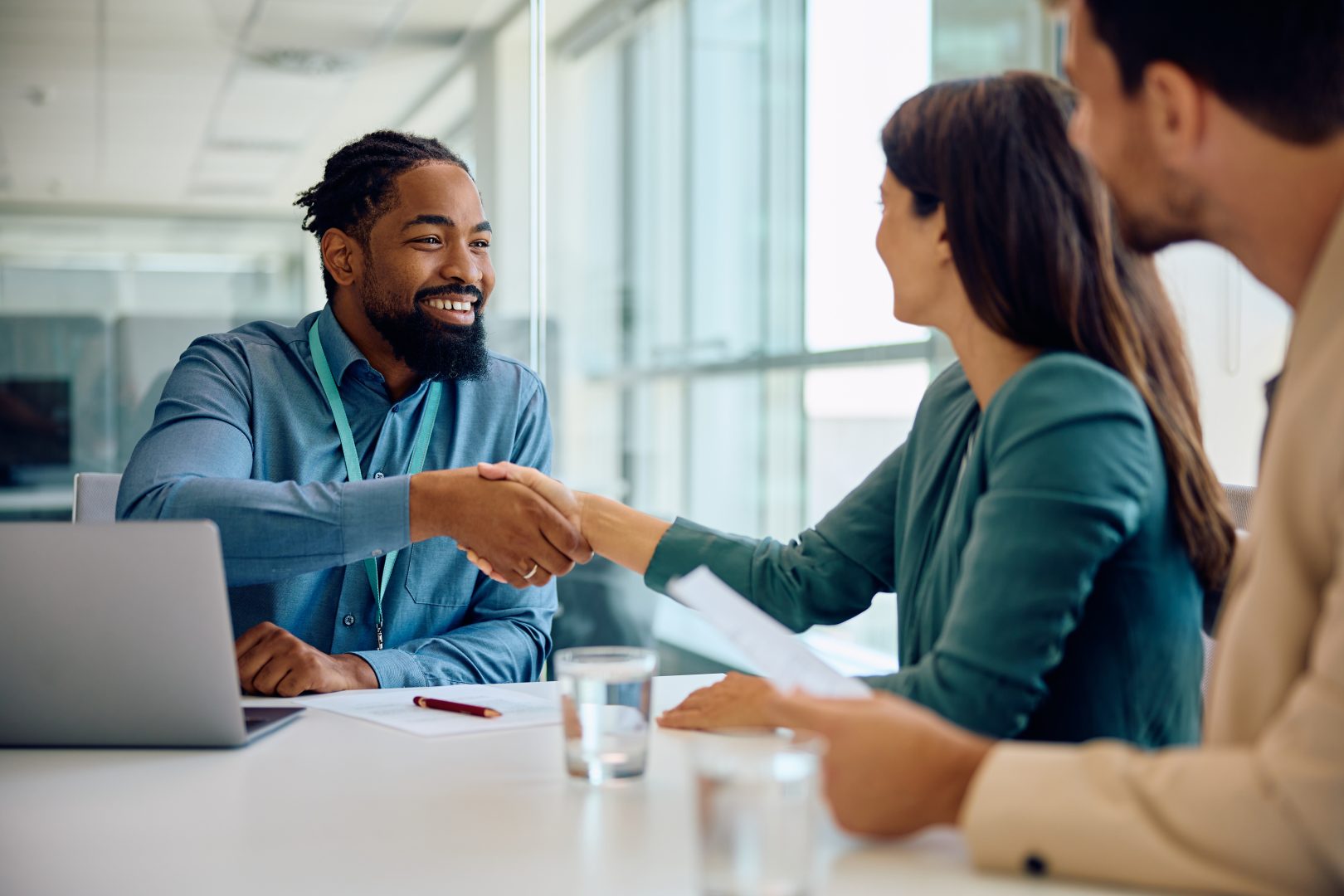 Happy black financial advisor handshaking with his clients during meeting in office.